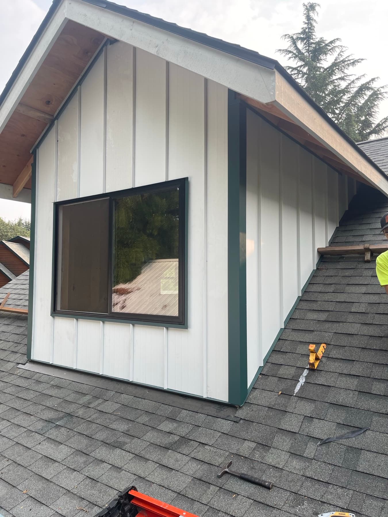 White-sided dormer with a black-framed window rising from a dark shingle roof