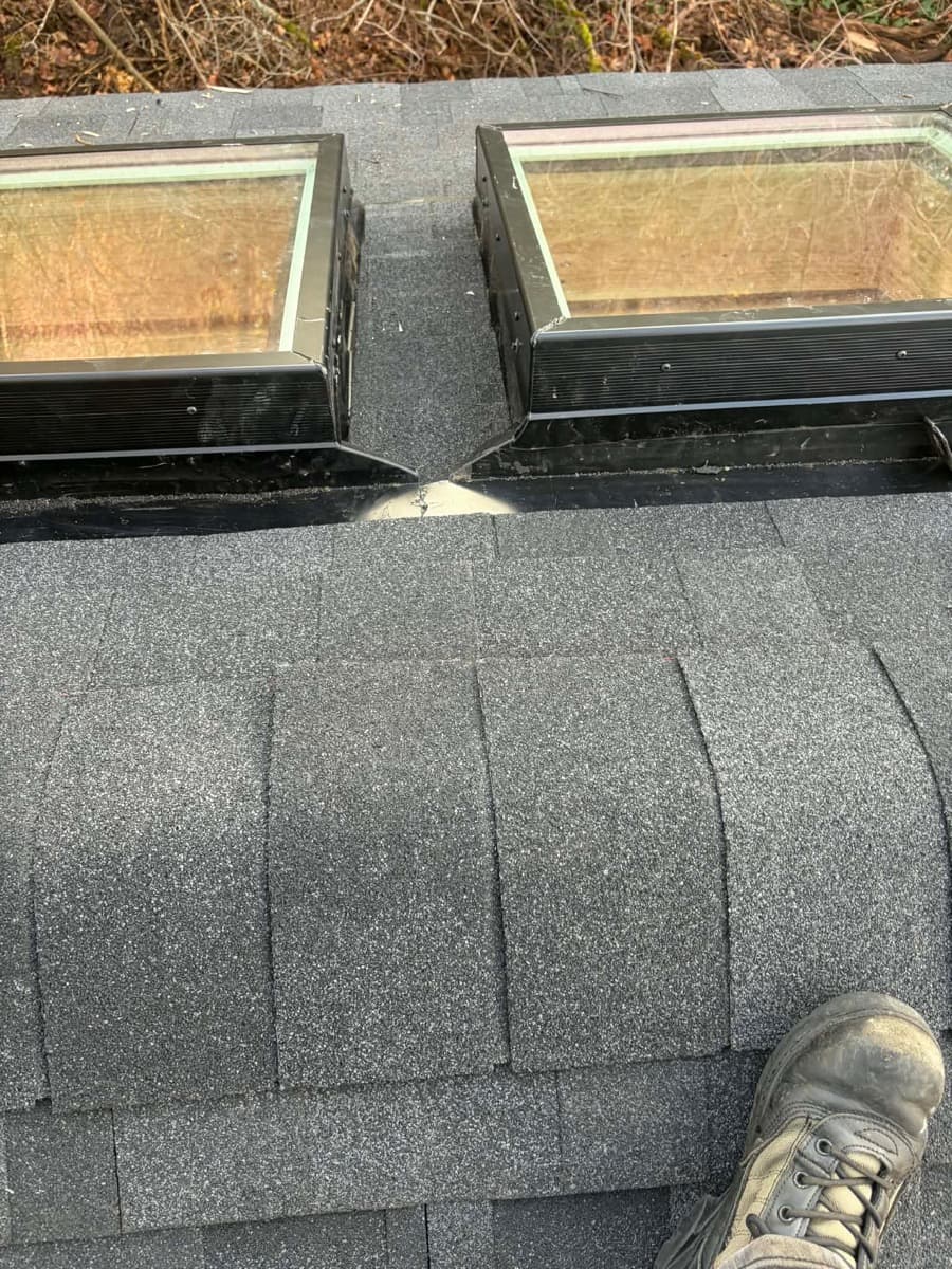 Two skylights set above a row of ridge shingles on a dark roof