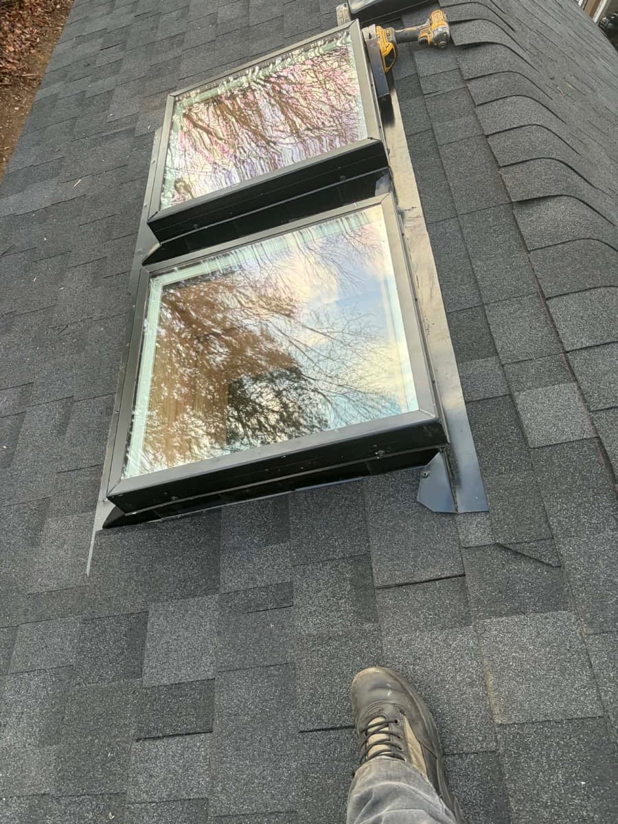 Two skylights with metal flashing set into a dark shingle roof