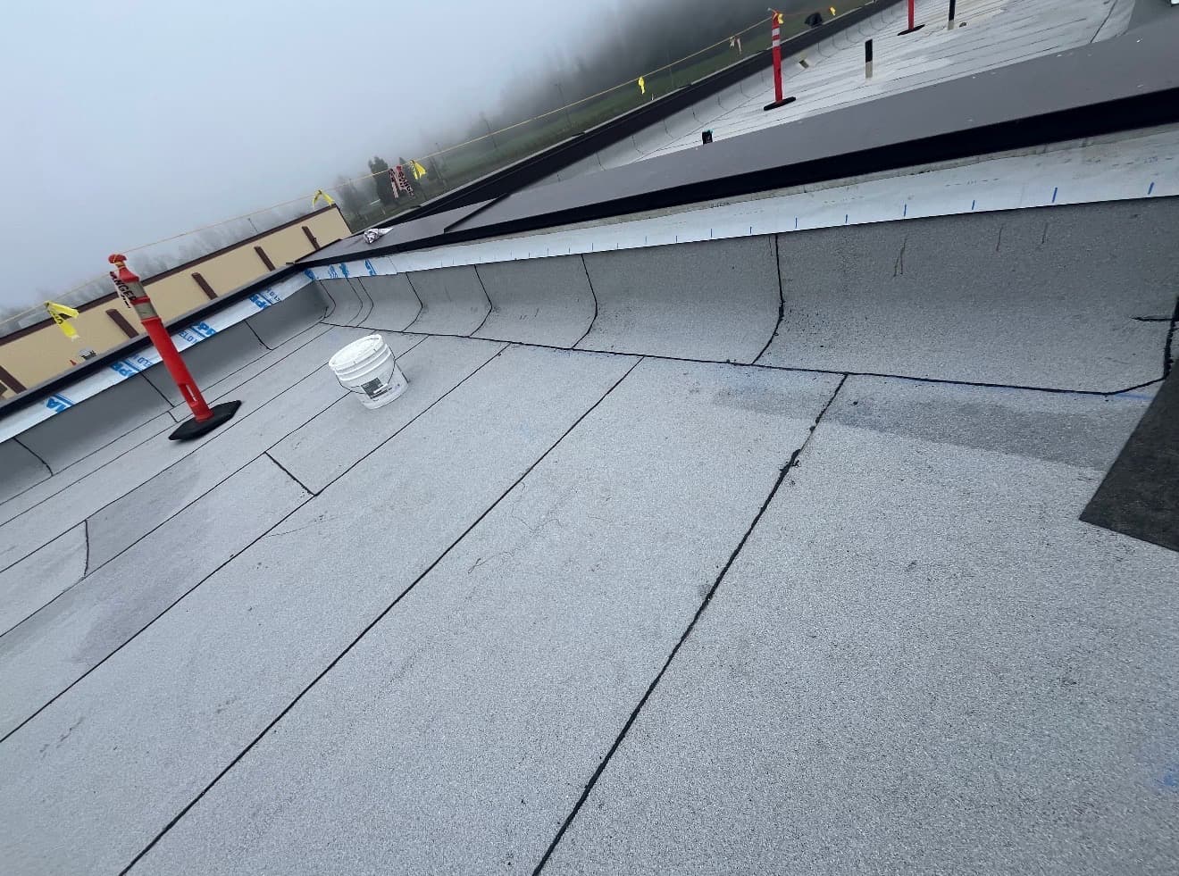 Flat modified bitumen roof with a raised curb, safety cones and a bucket on the membrane