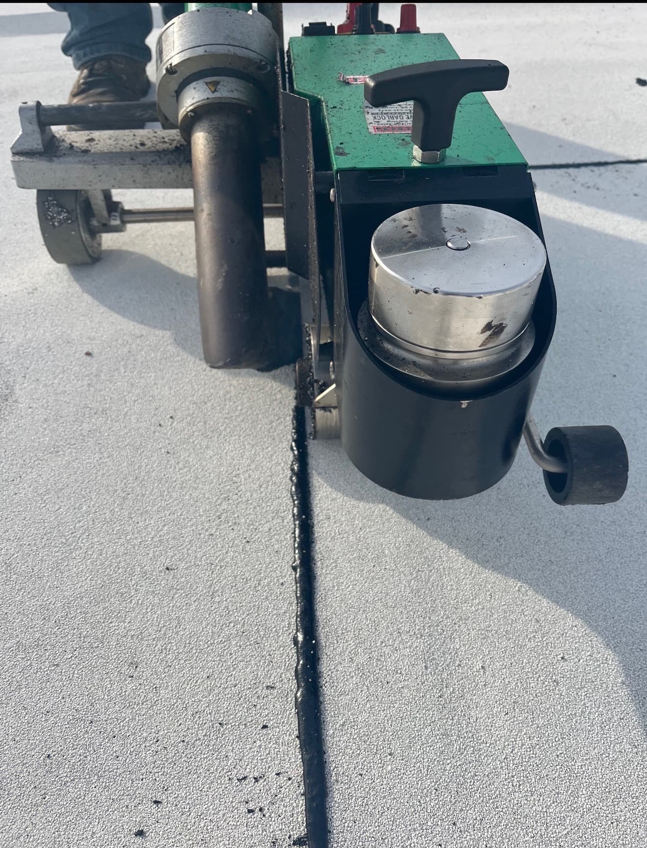 Automatic heat welder running along a seam on a gray flat roof membrane