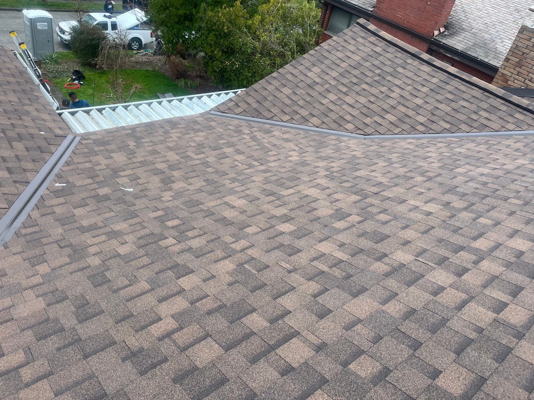 Brown shingle roof planes meeting at a valley, with a neighboring roof beyond
