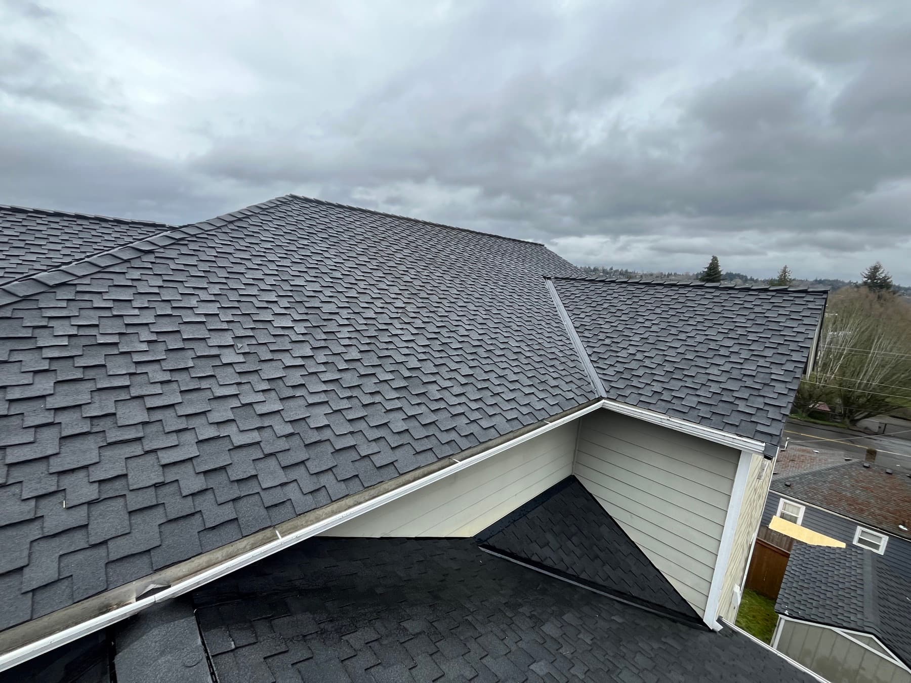 Dark shingle roof with a gabled section under a heavy overcast sky