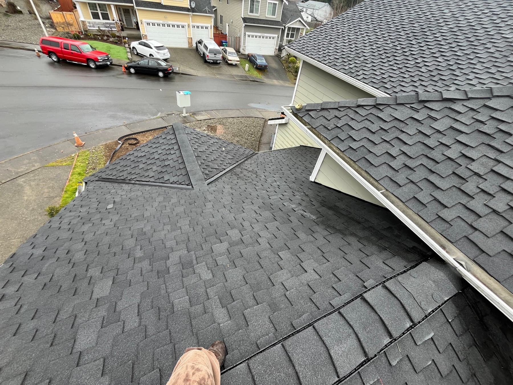 Dark gray shingle roof with a hip and valley, seen from above a residential street