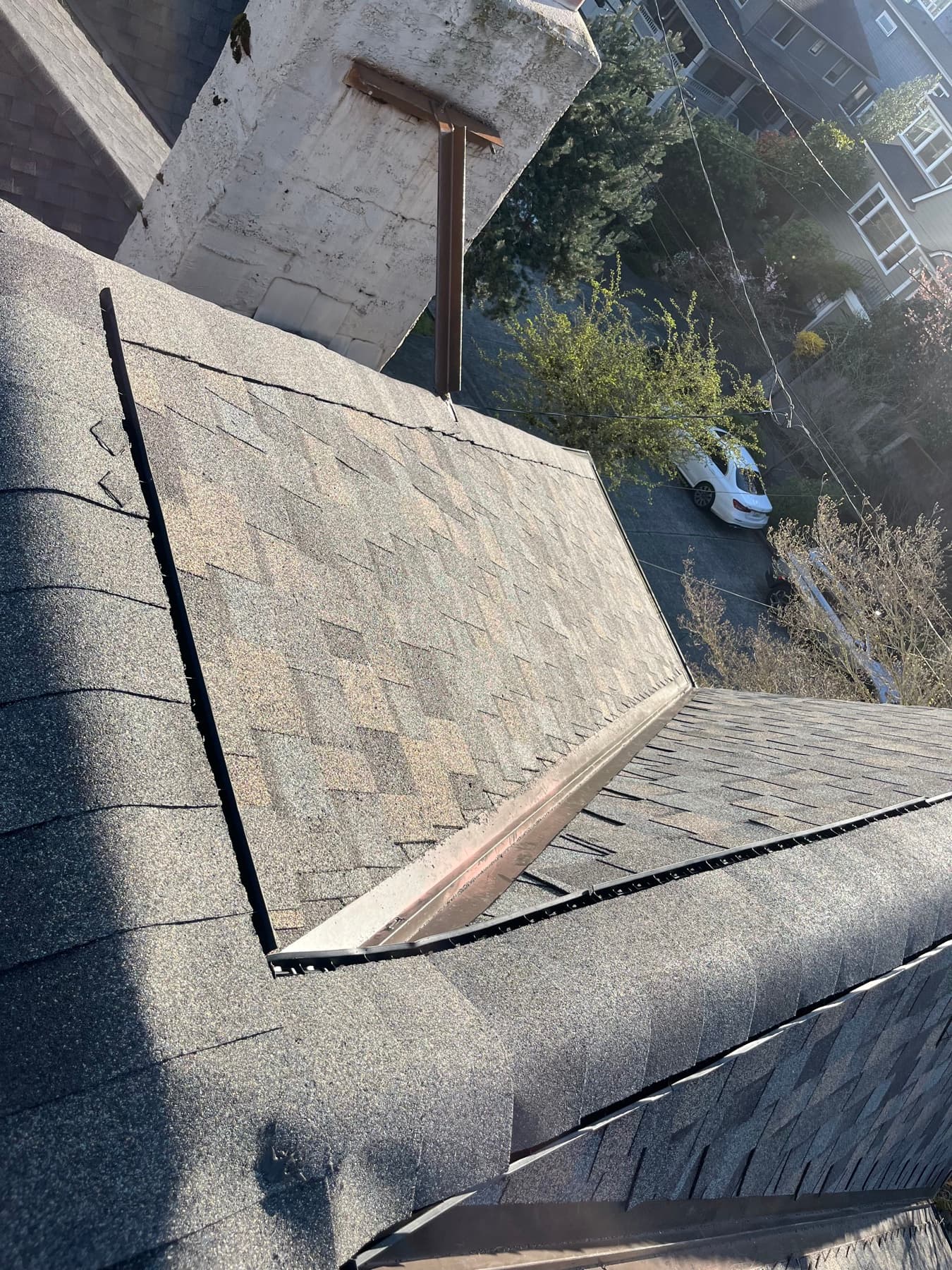 Aerial view of a chimney, flashing and shingle ridges on a tan roof among trees